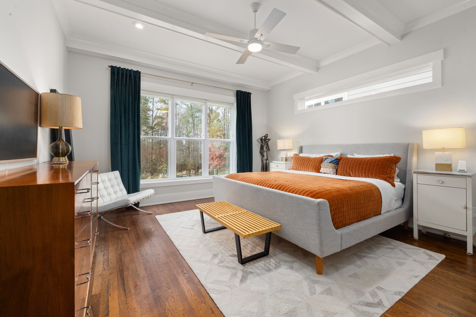 A luxury master bedroom with high-end linens, warm natural light, and styled seating.