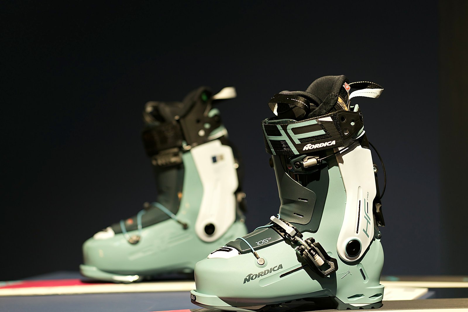 Close view of sage Nordica ski boots on a dark fitting display.