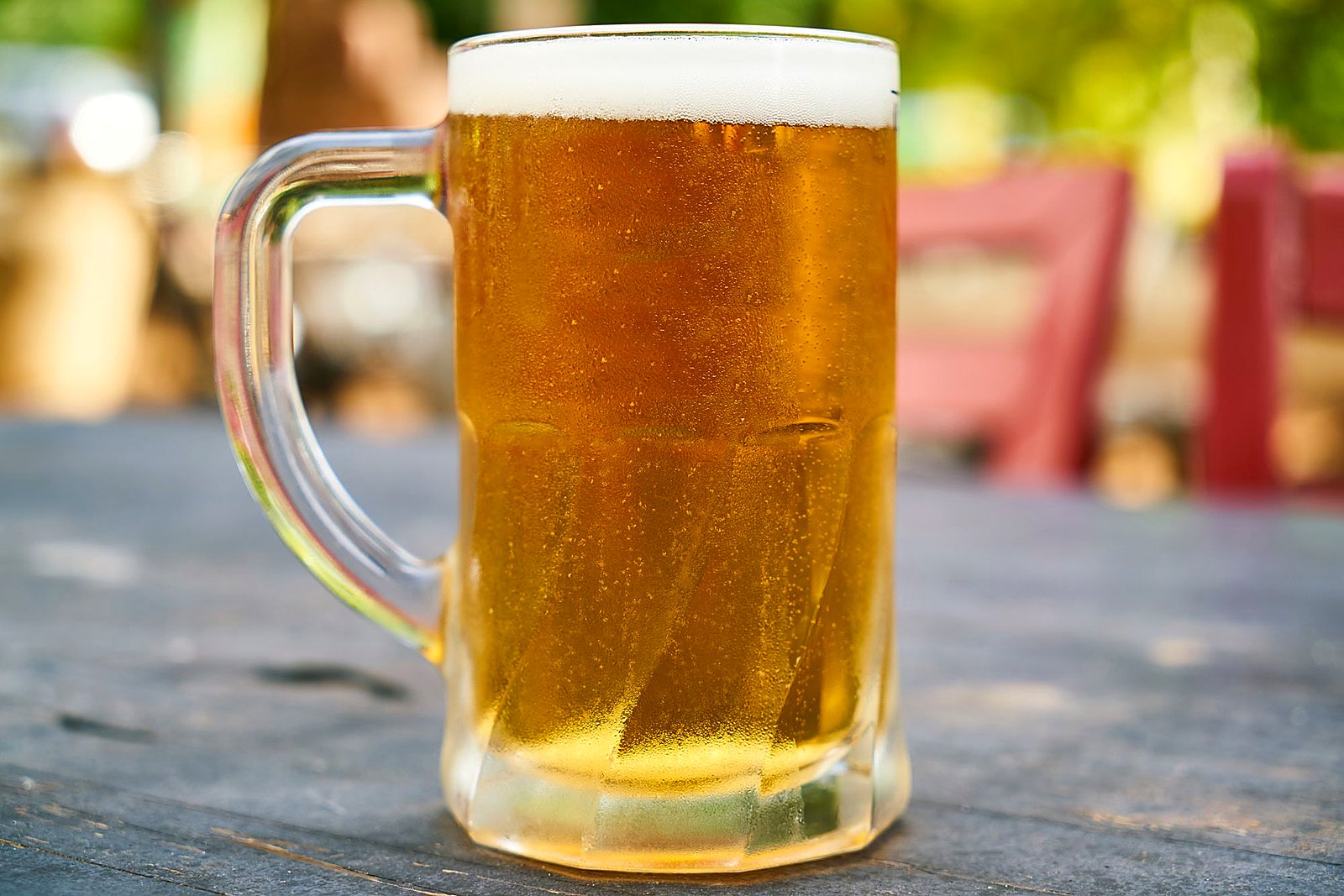 Golden craft beer mug with condensation on a wooden patio table in sunlight.