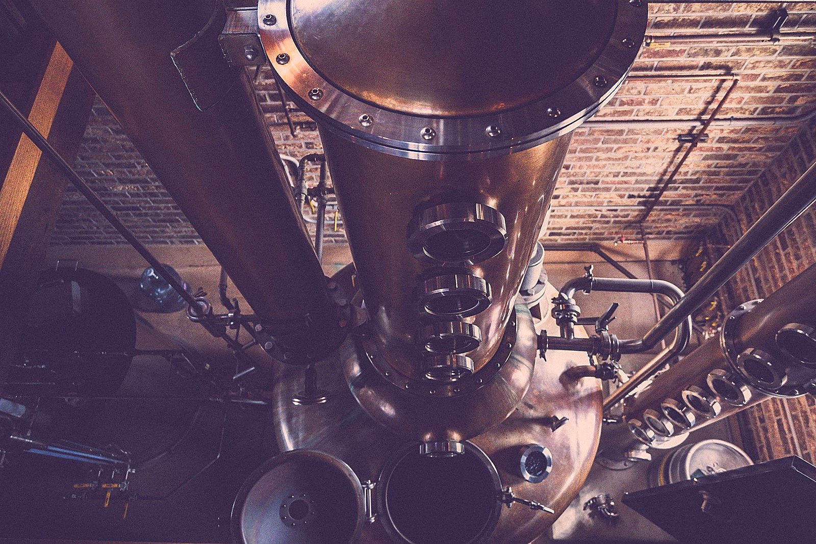 Top-down view of polished copper still columns with sight glasses against brick.