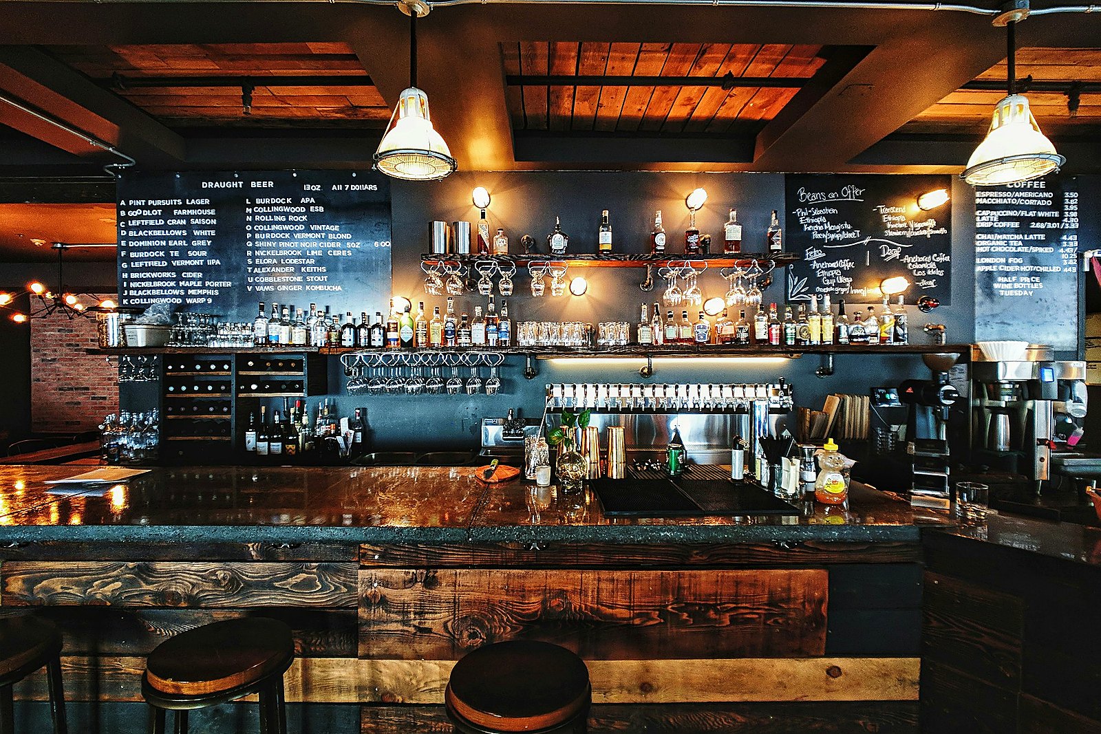 Warm wooden taproom bar with a long draught tap rail and pendant lights.