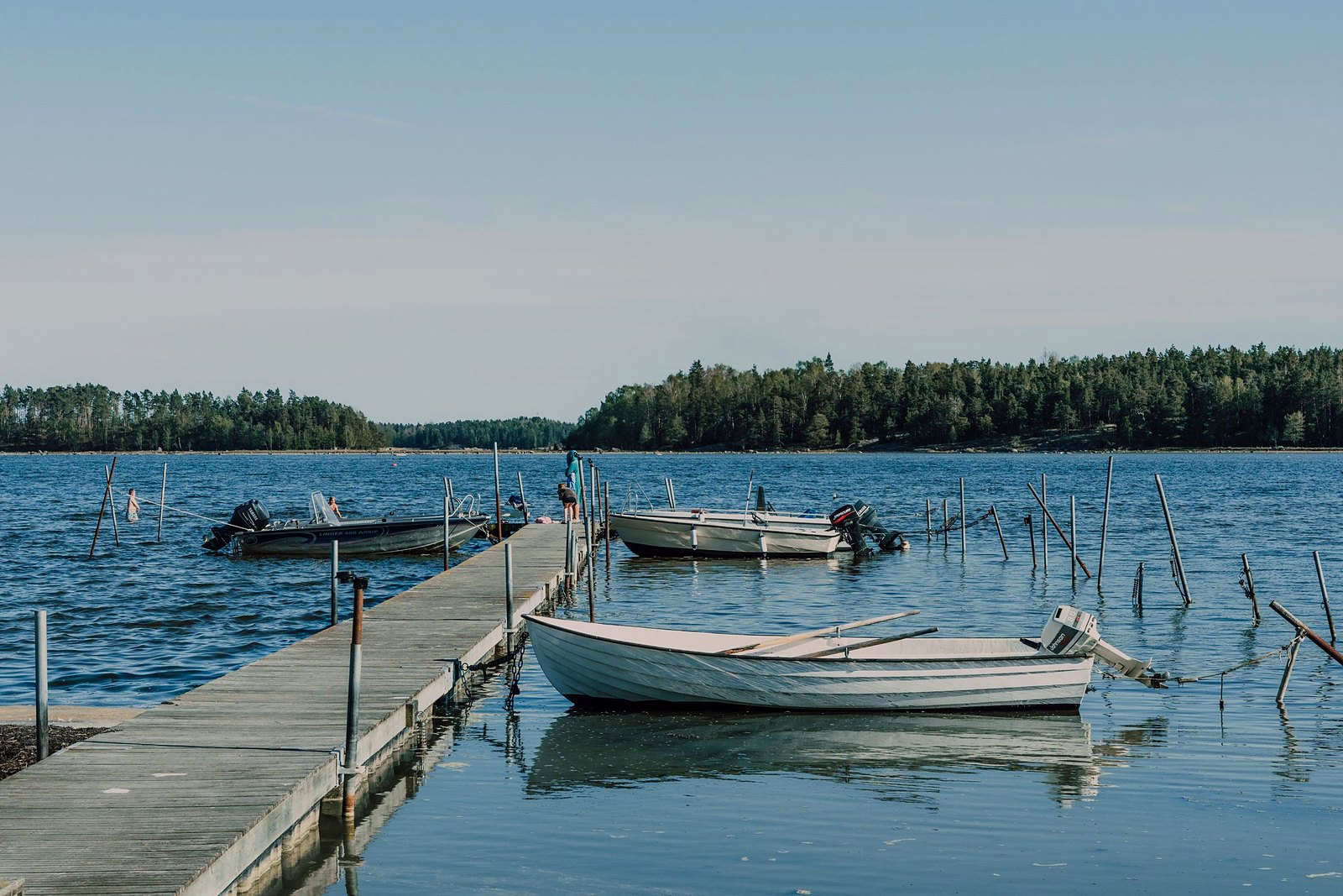 Utility boat tied to a wooden pier on clear blue lake water with trees beyond.