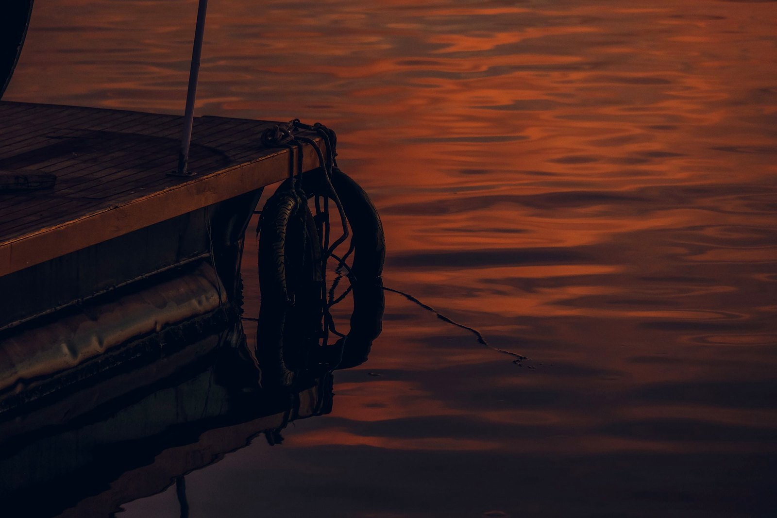 Lifebuoy on a weathered wooden dock edge with sunset reflecting on the water.