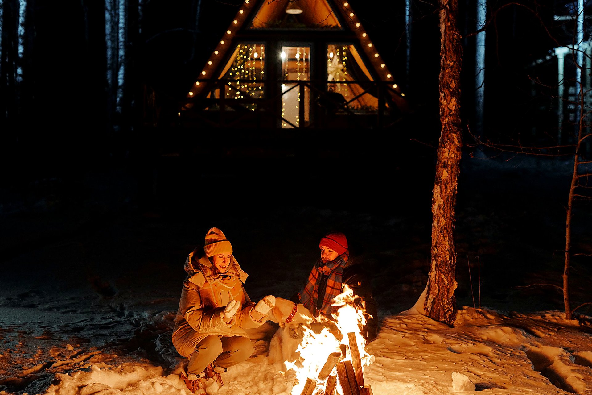 Campfire and glowing A-frame cabin on a snowy night after the ice.