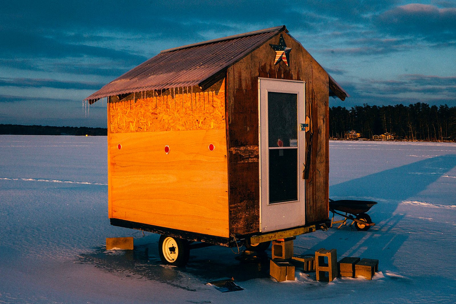 Wooden ice fishing shanty glowing in golden hour light on a frozen lake.