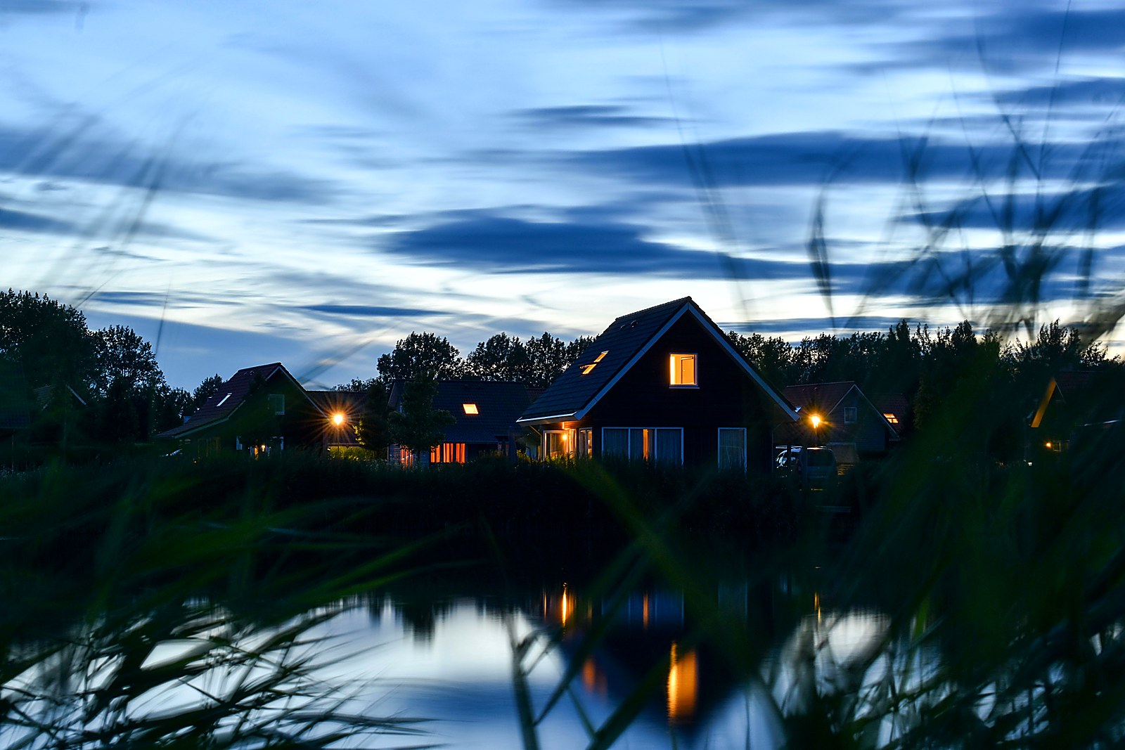 Dark-sided lake houses with warm window lights glowing at blue hour by the water.