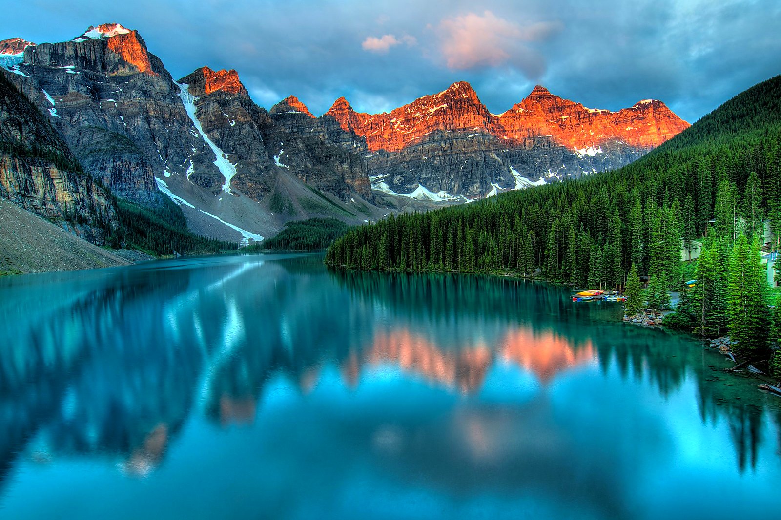 Calm turquoise mountain lake at dawn with pine forest reflecting on still water.