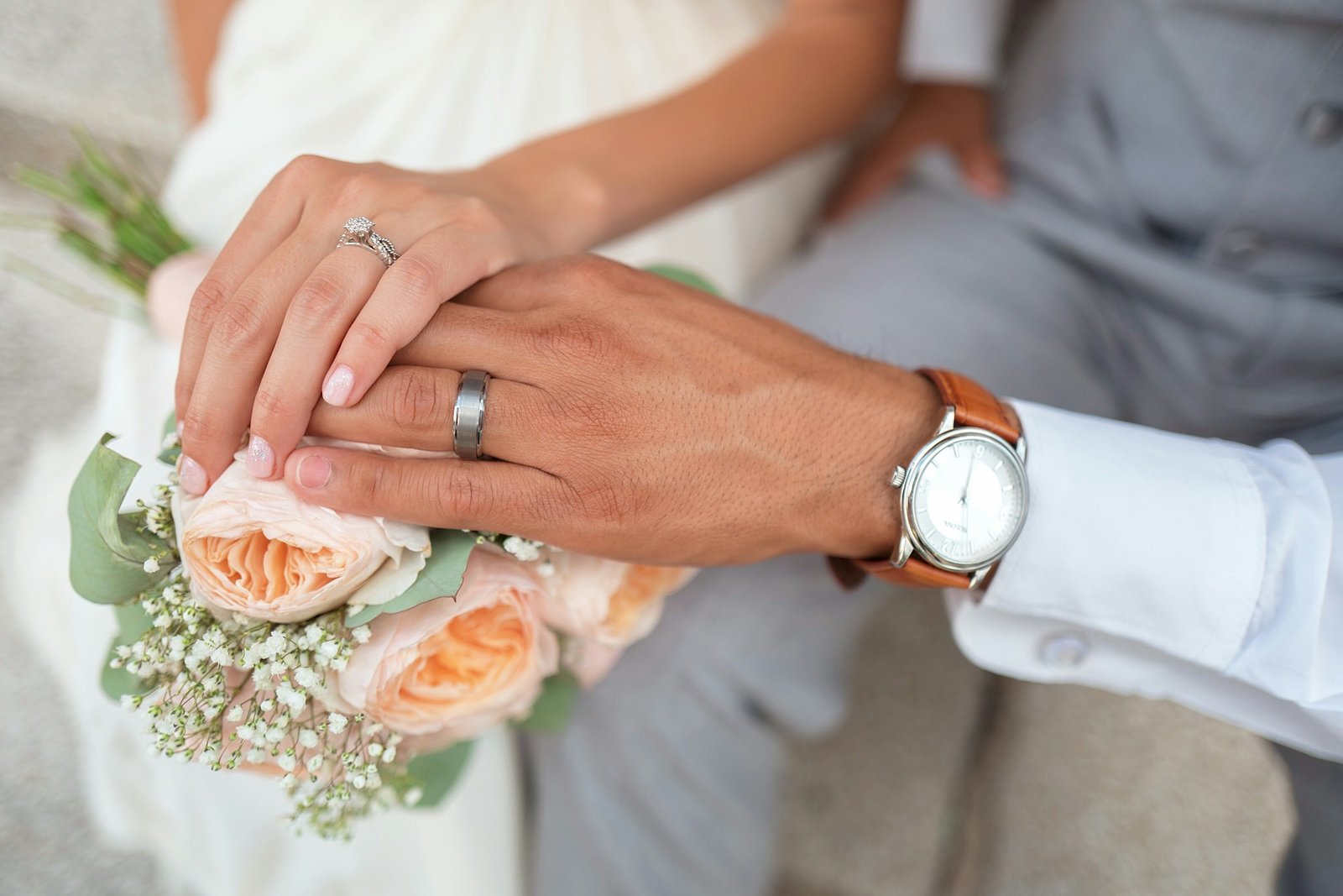 Joined hands resting on a peach rose bouquet.