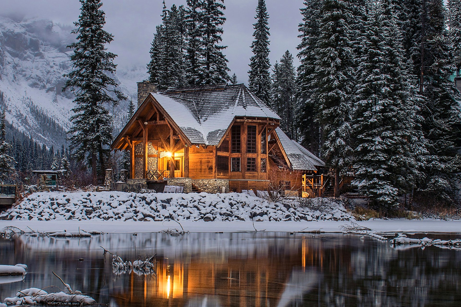 Snowy lakeside timber lodge glowing with warm window light at twilight.