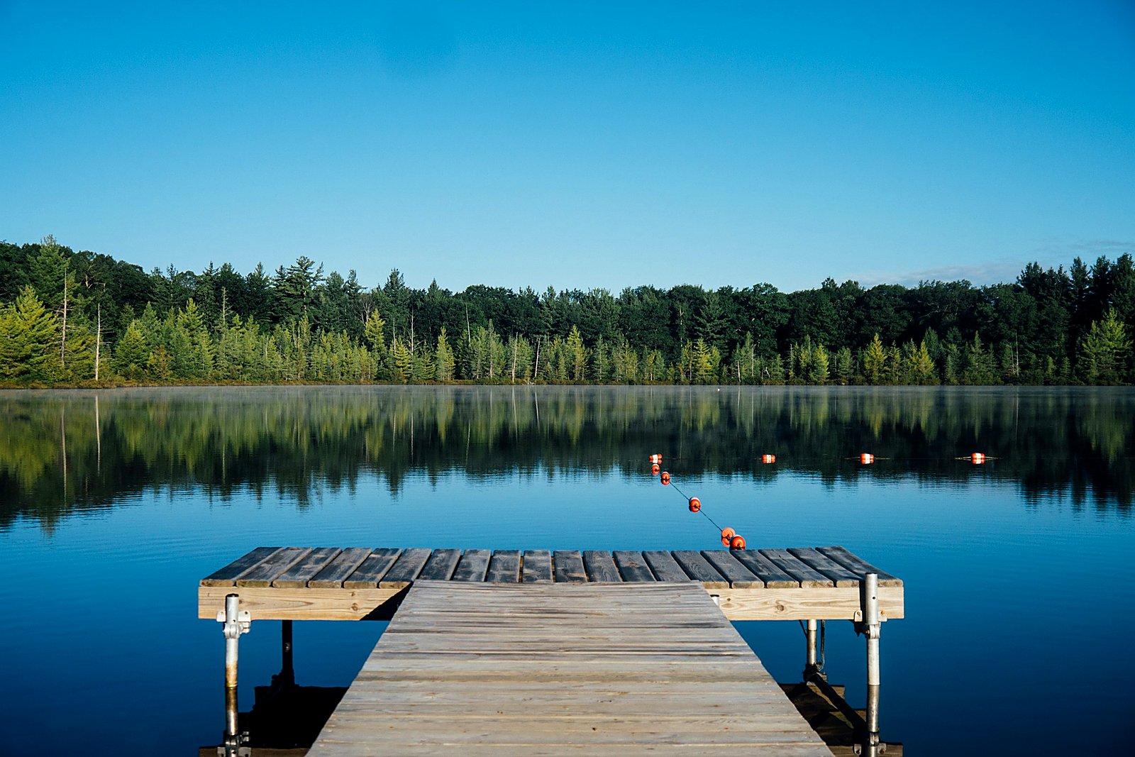 Wooden dock on a calm Maine lake with morning mist along the far shore.