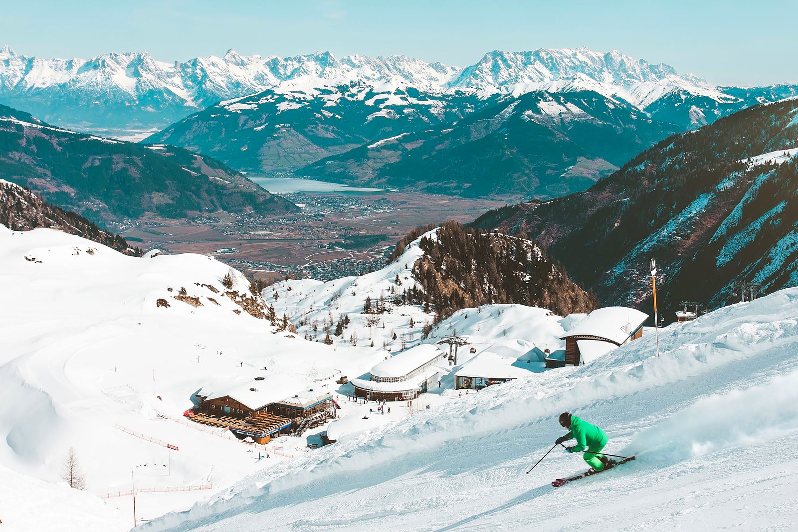 Skier carving a groomed alpine trail with mountain peaks beyond.