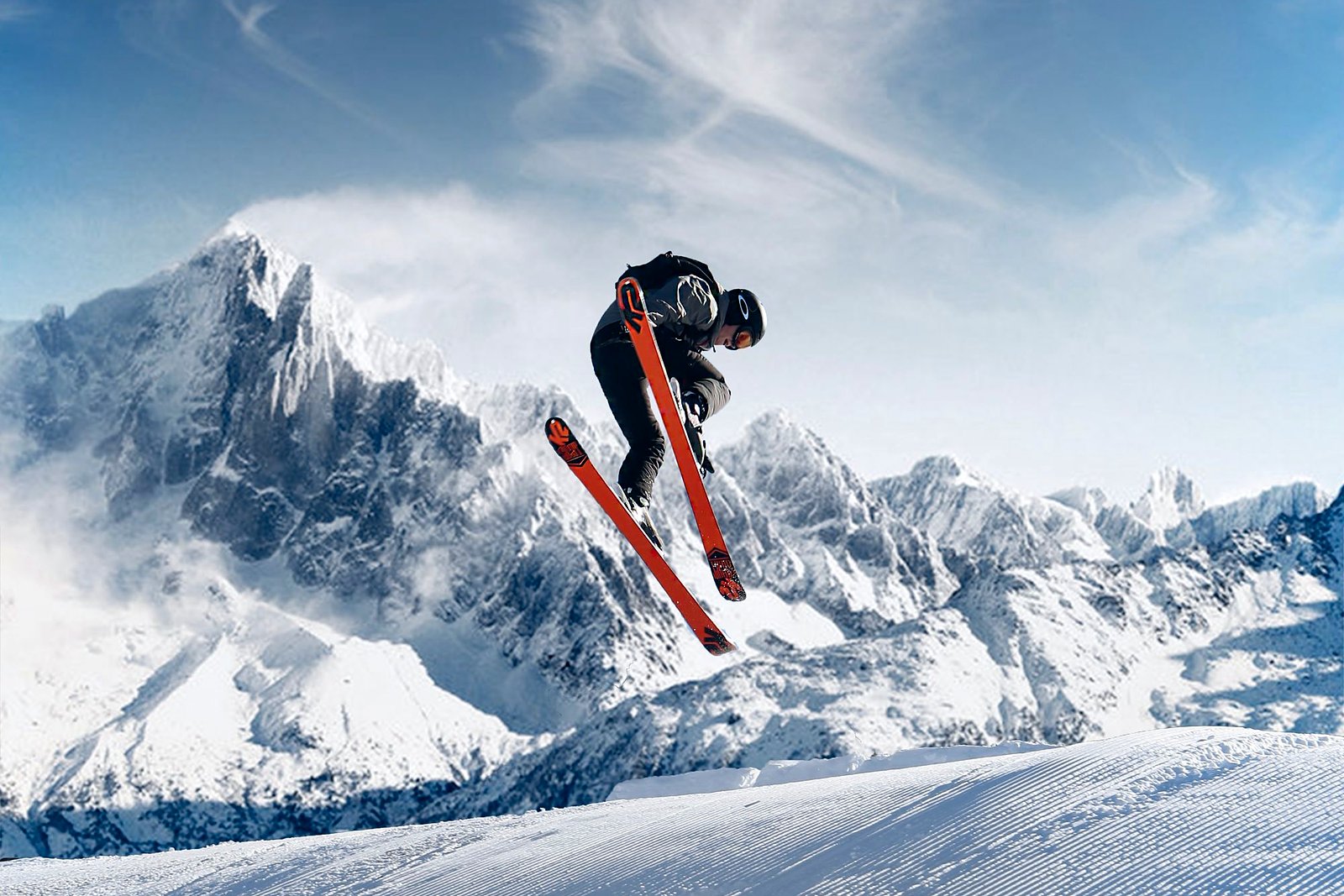 Skier jumping above corduroy with orange skis against blue sky.