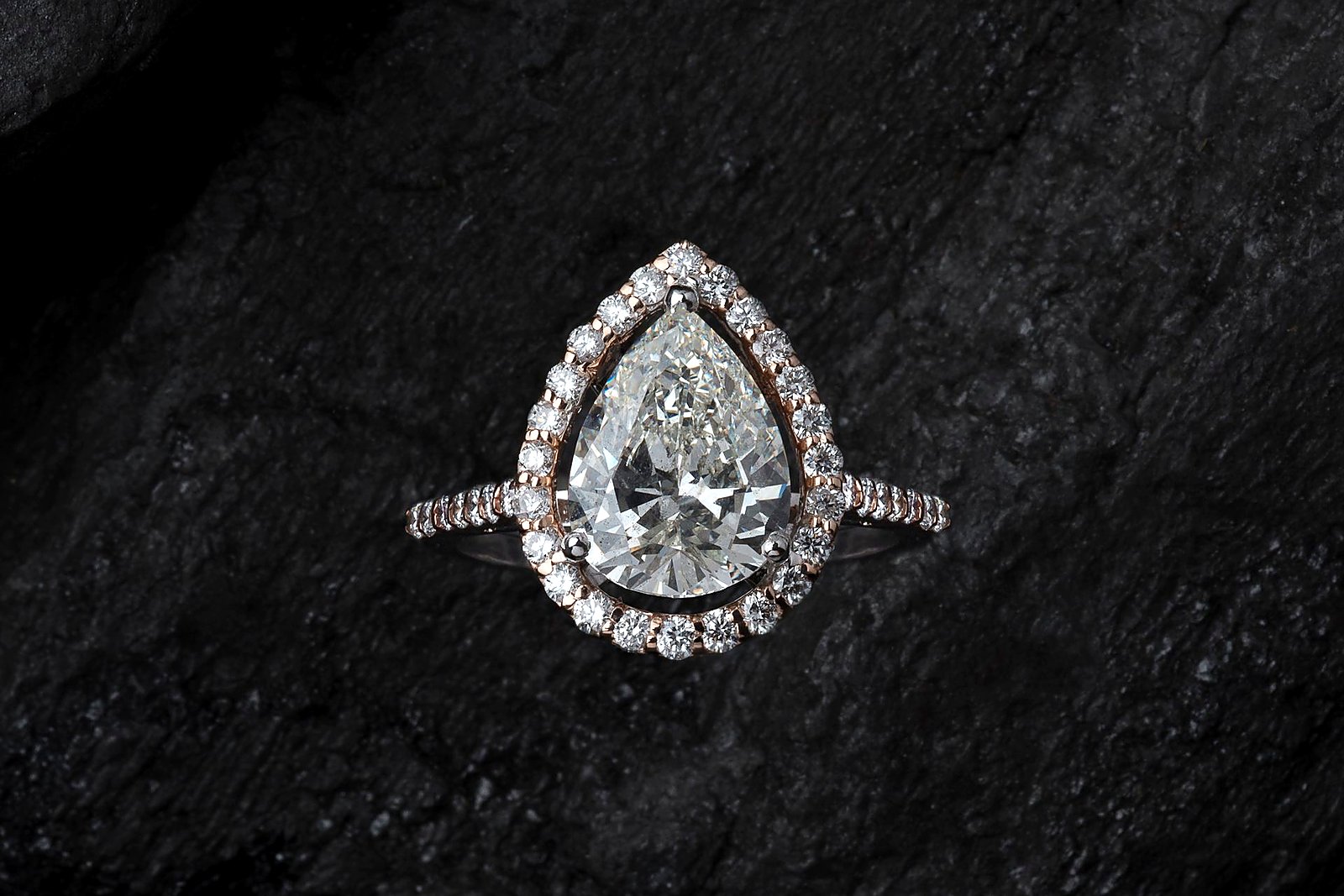 Pear-cut diamond engagement ring with halo resting on dark textured stone.