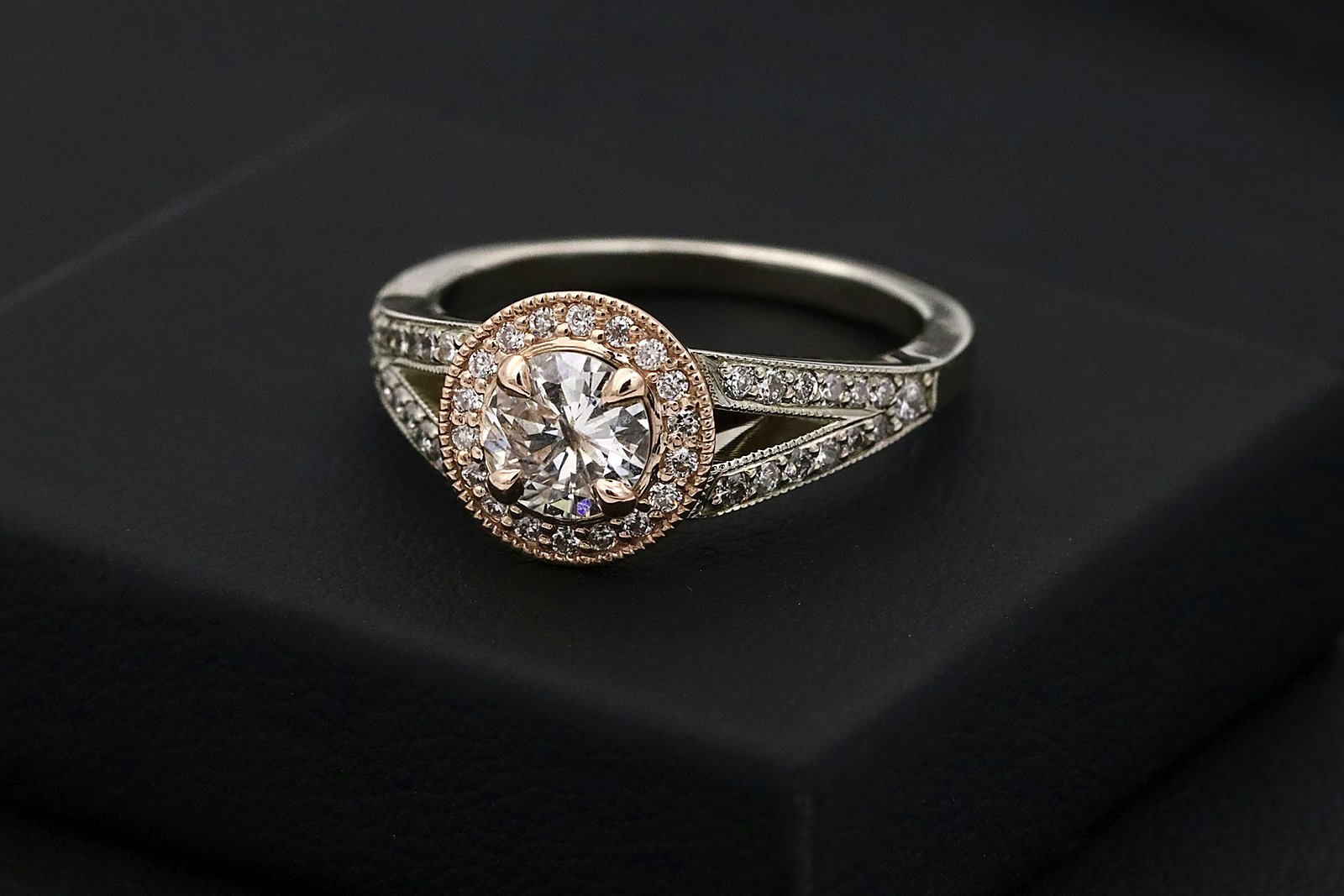 Rose-gold halo diamond engagement ring on a dark presentation surface.