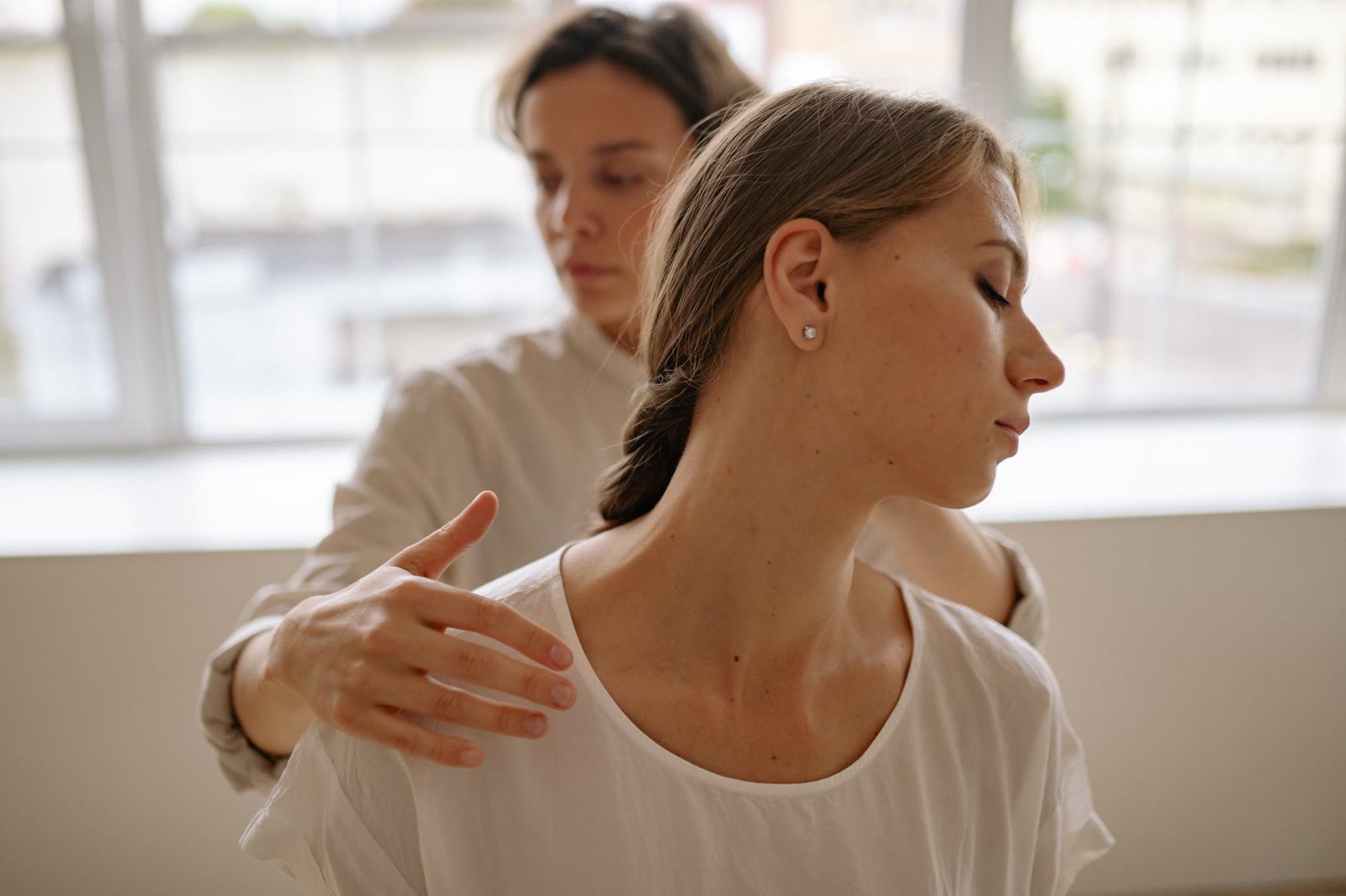 Therapist hands gently on a client's shoulder in soft daylight.