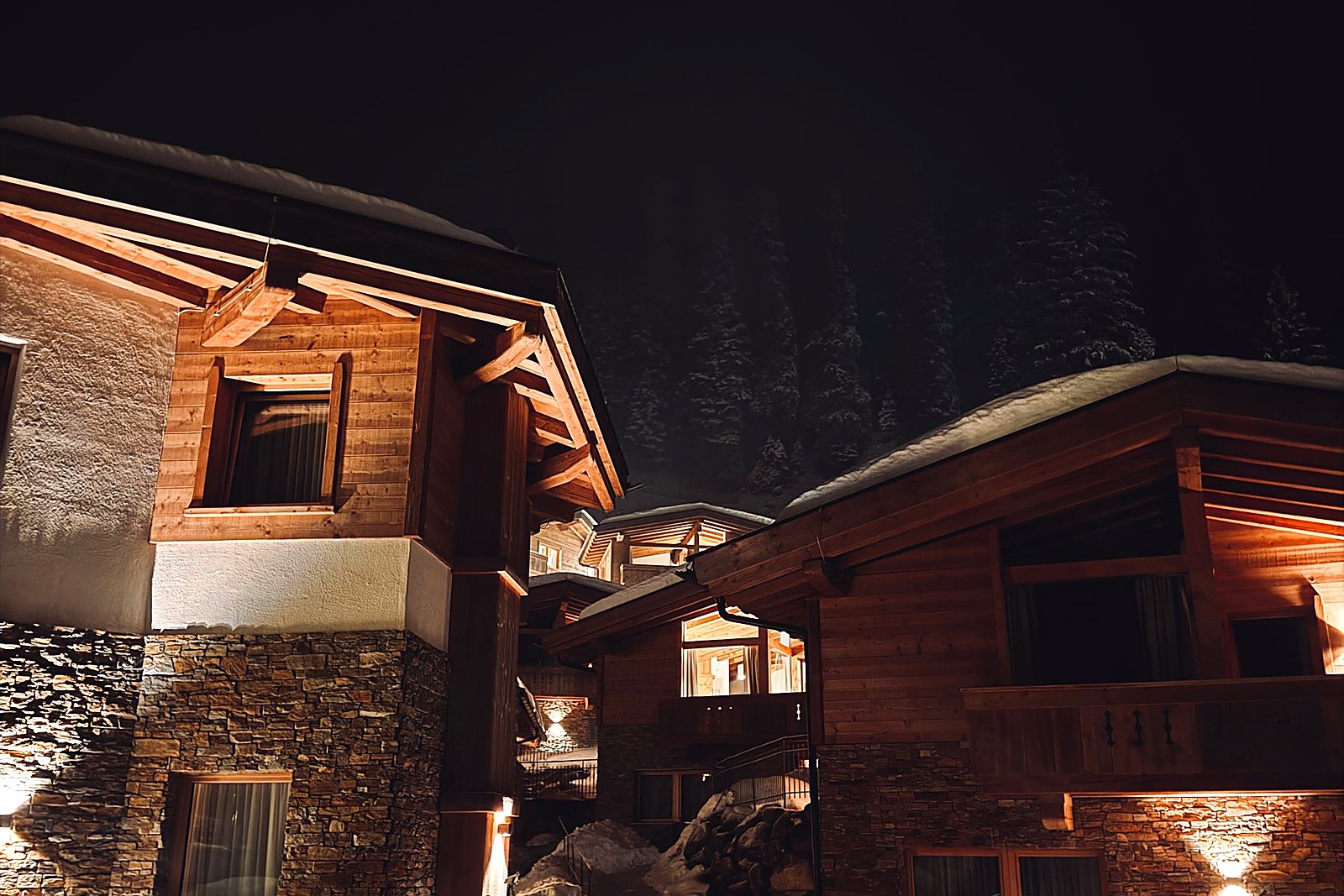 Warm-lit stone and timber houses at night with cleared snow walkways.