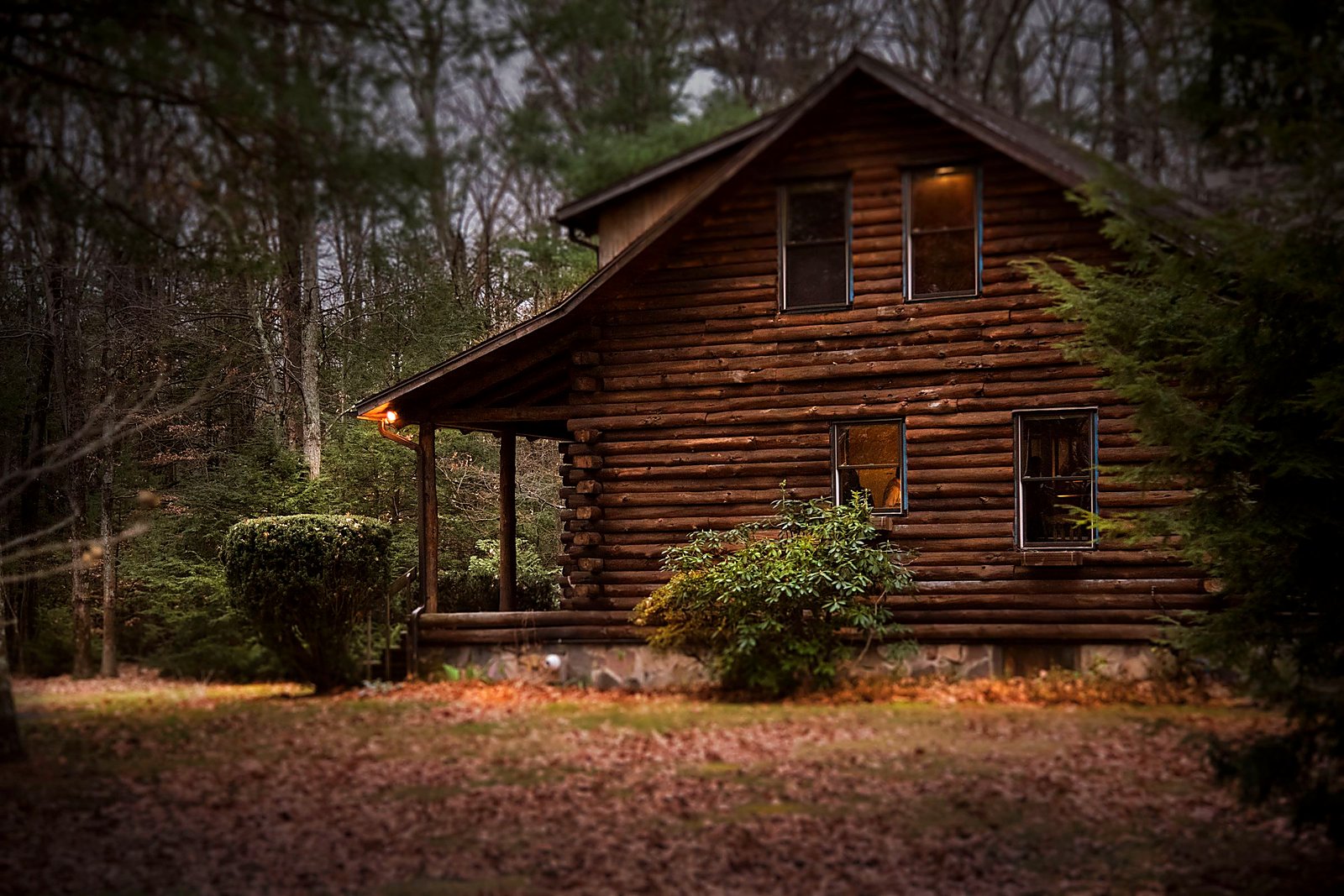 Log cabin with warm porch light glowing at dusk.